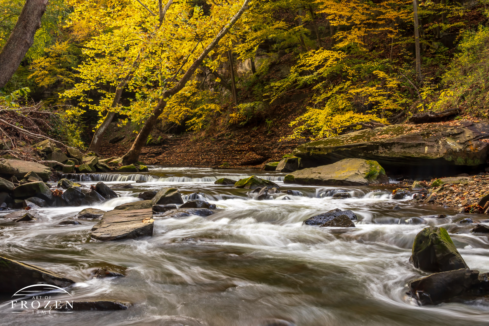 As Trinker's Creek flows through its gorge, the water flows over a series of small waterfalls as the water swirls around large boulders on a fall day