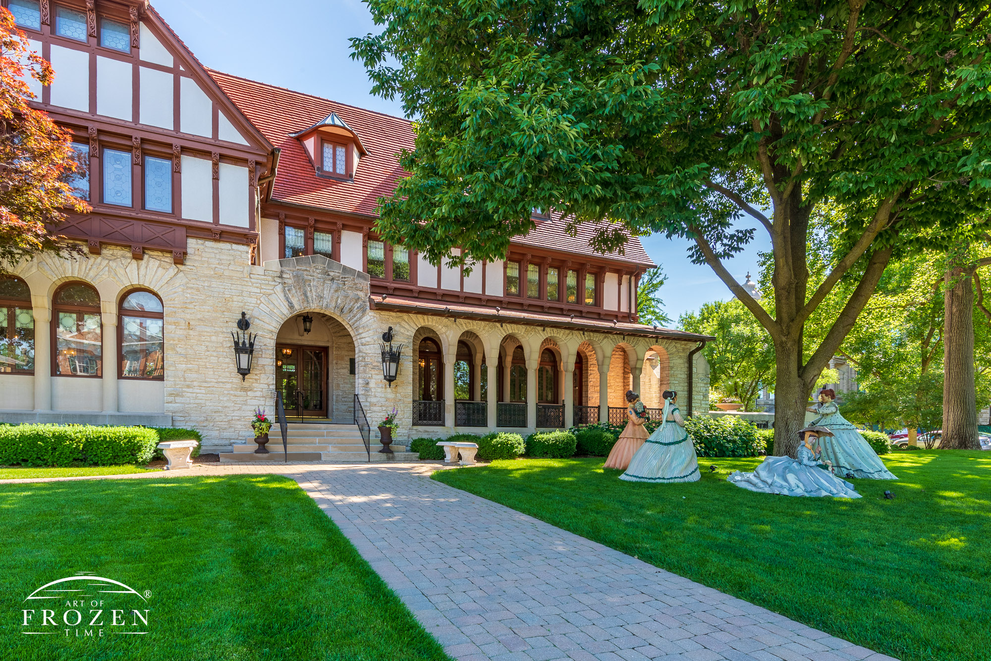 The Troy-Hayner Cultural Center resides in a home featuring Romanesque architecture such as this exterior view where sunlight washes over the stone facade and tile work and surrounding trees provide cool shade