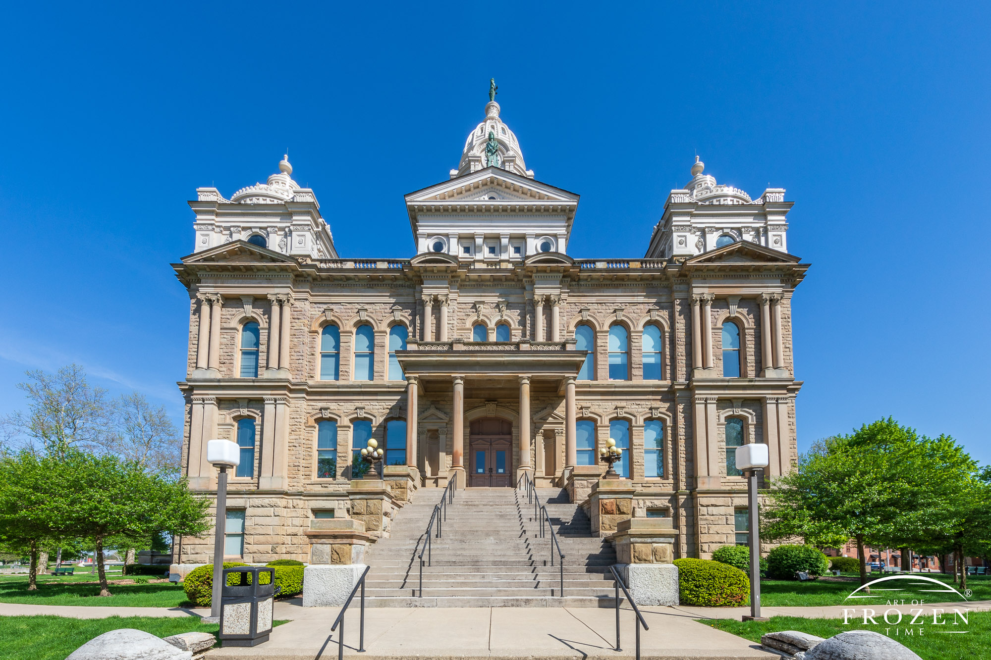 A dayttime view of the Miami County, Ohio Courthouse showing its Corinthian columns and ornate facade in the warm spring light.