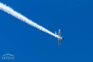Aerobatic airplane flying vertical before leveling offer while leaving a bright white contrail in a clear blue sky