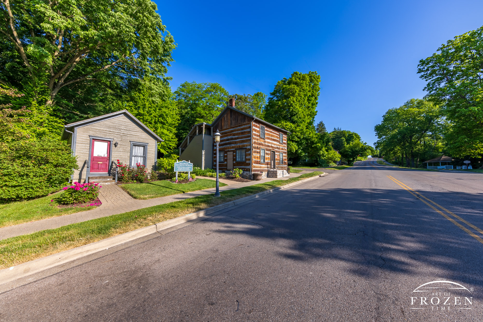A Greene County historical structure where a refurbished log home stands in Bellbrook, Ohio under blue skies and at the bottom of Main Street which descends into the village