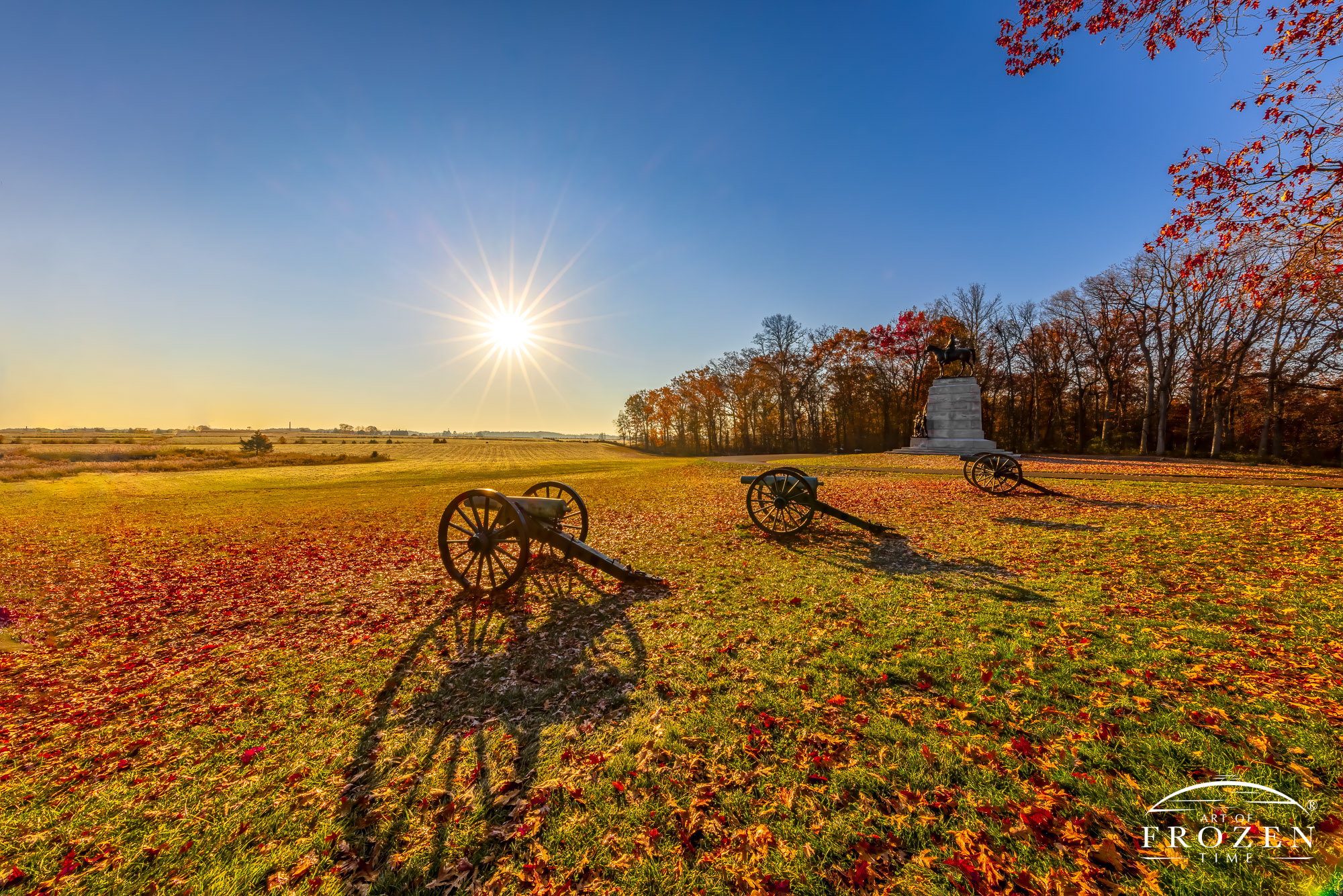 A battery of Civil War cannons at Gettysburg National Military Park on an autumn morning while a monument to Virginia lies in the distance.