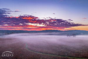 Aerial view of Morris Reserve near Bellbrook Ohio with prairie path disappearing into fog beneath colorful orange and pink sunrise clouds