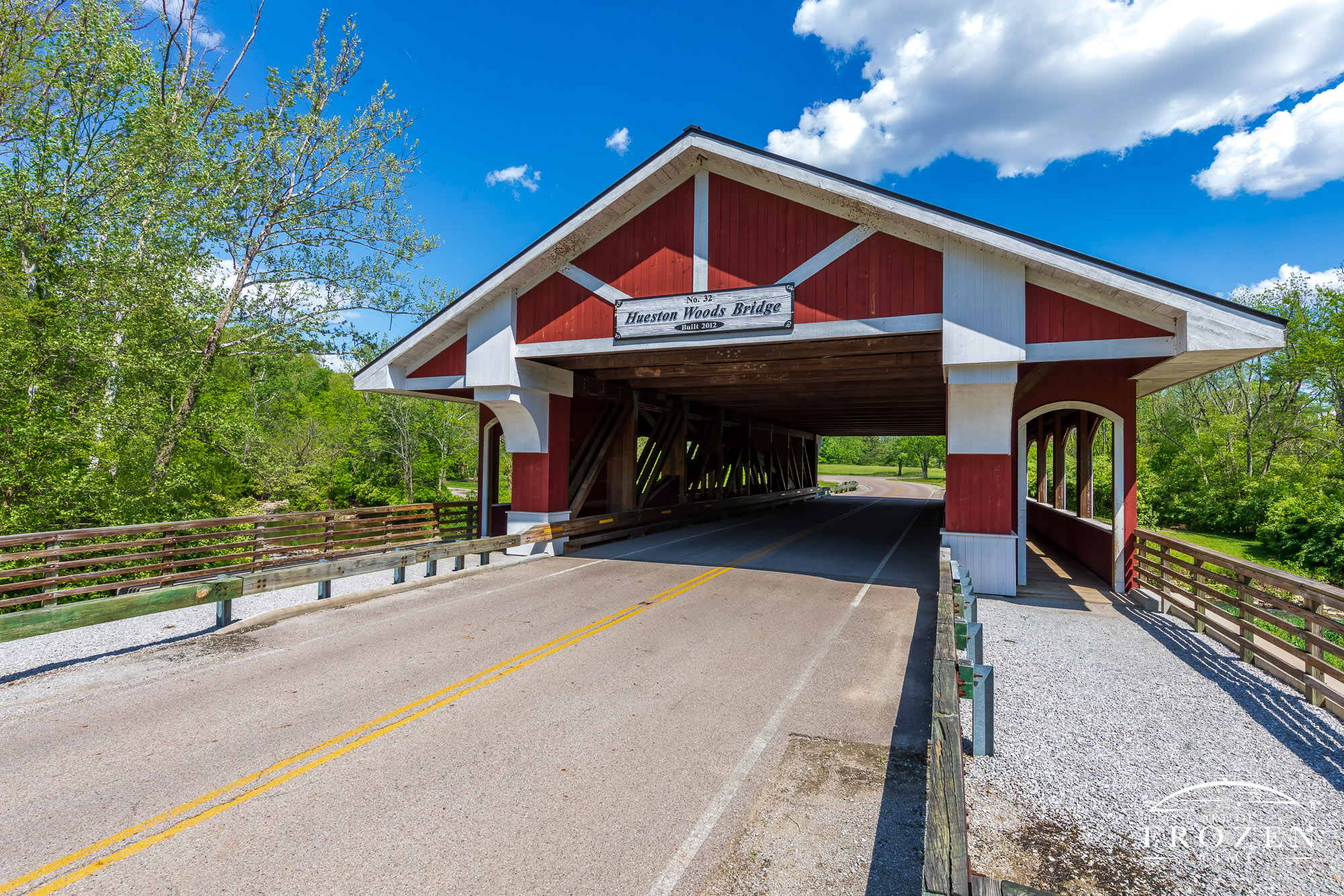 An Ohio covered bridge painted red with white accents basks in the daylight on a pretty spring day