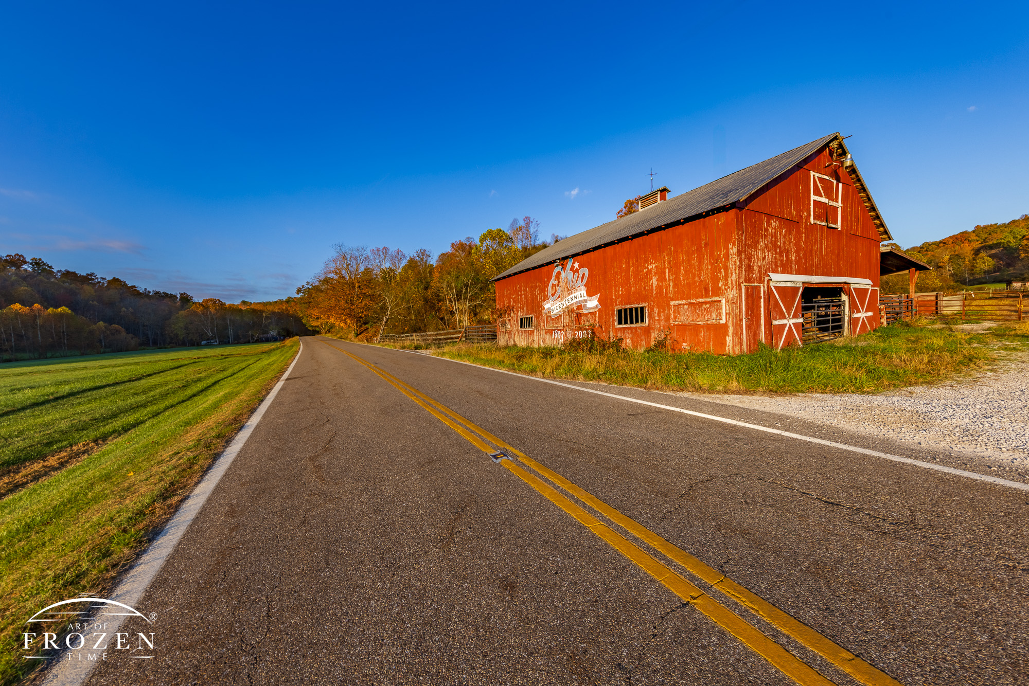 The Lawrence County Ohio Bicentennial Barn, originally restored and painted in 2000, now shows signs of age as its patriotic Ohio logo fades. Bathed in golden autumn light, the historic red barn stands along a quiet country road in Appalachian Ohio.