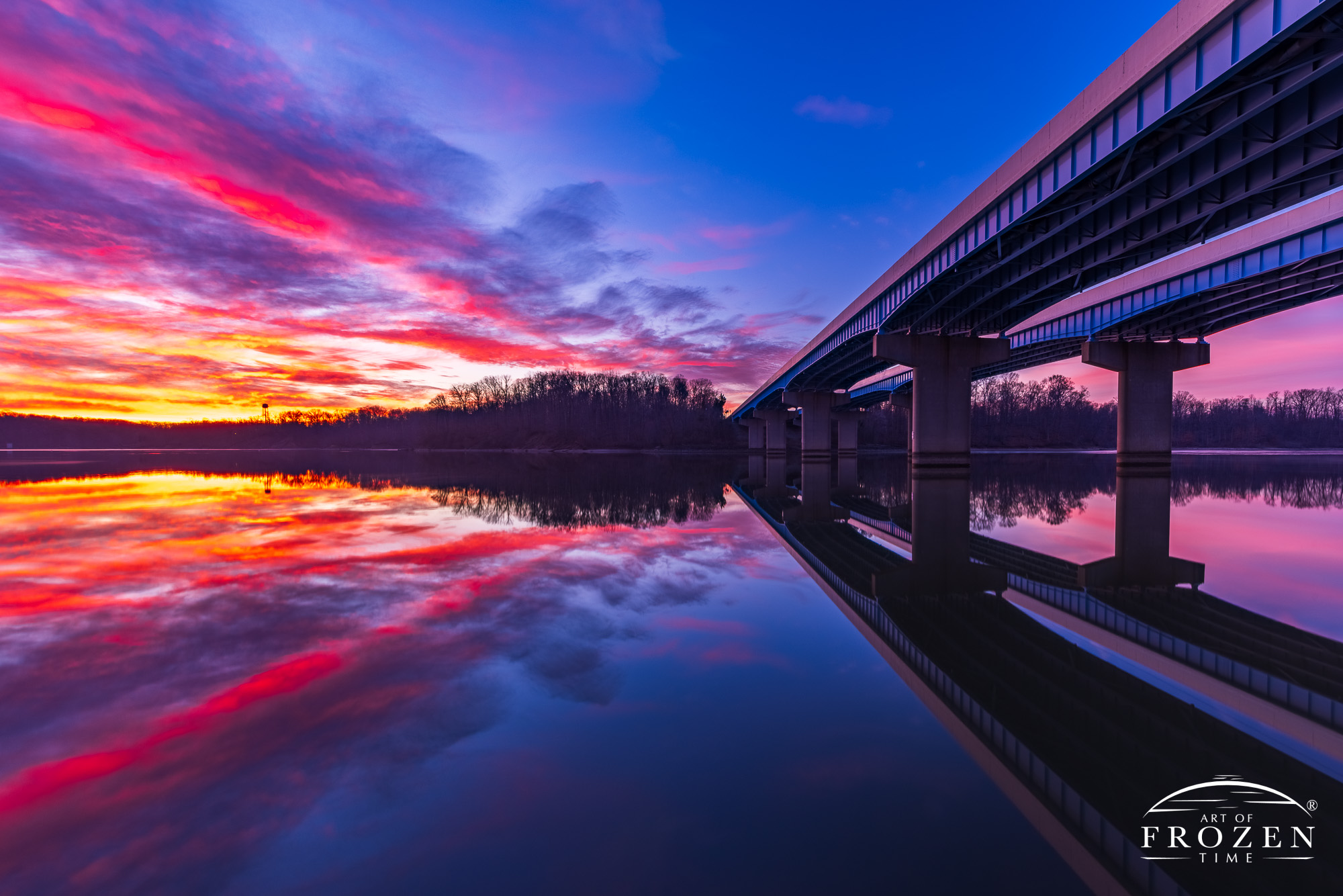 A colorful fine art print featuring a band of serendipitous clouds at sunrise which perfectly mirrored a bridge crossing the Caesar Creek reservoir