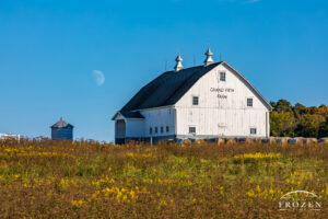 White barn at McCafferty Grand View Farm near Fayetteville in Brown County, Ohio, with golden evening light, goldenrod, blue sky, and rising moon.