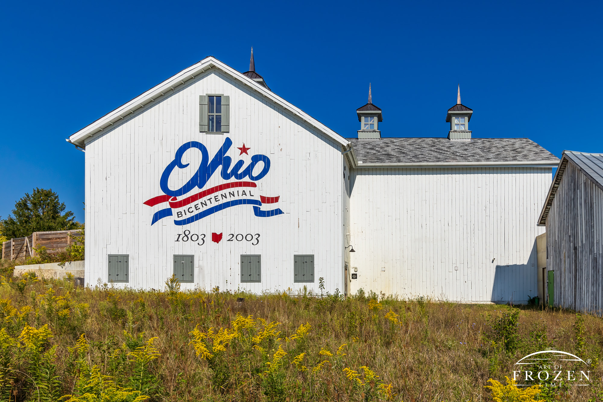 A fully restored 100-year old barn proudly displaying its Ohio Bicentennial Logo. The bright white paint glistened under the blue sky.