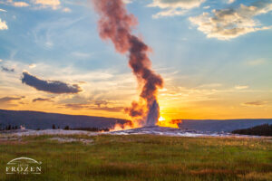 An evening view of Old Faithful at Yellowstone National Park where the sun backlights the geothermal sprays in warm colors