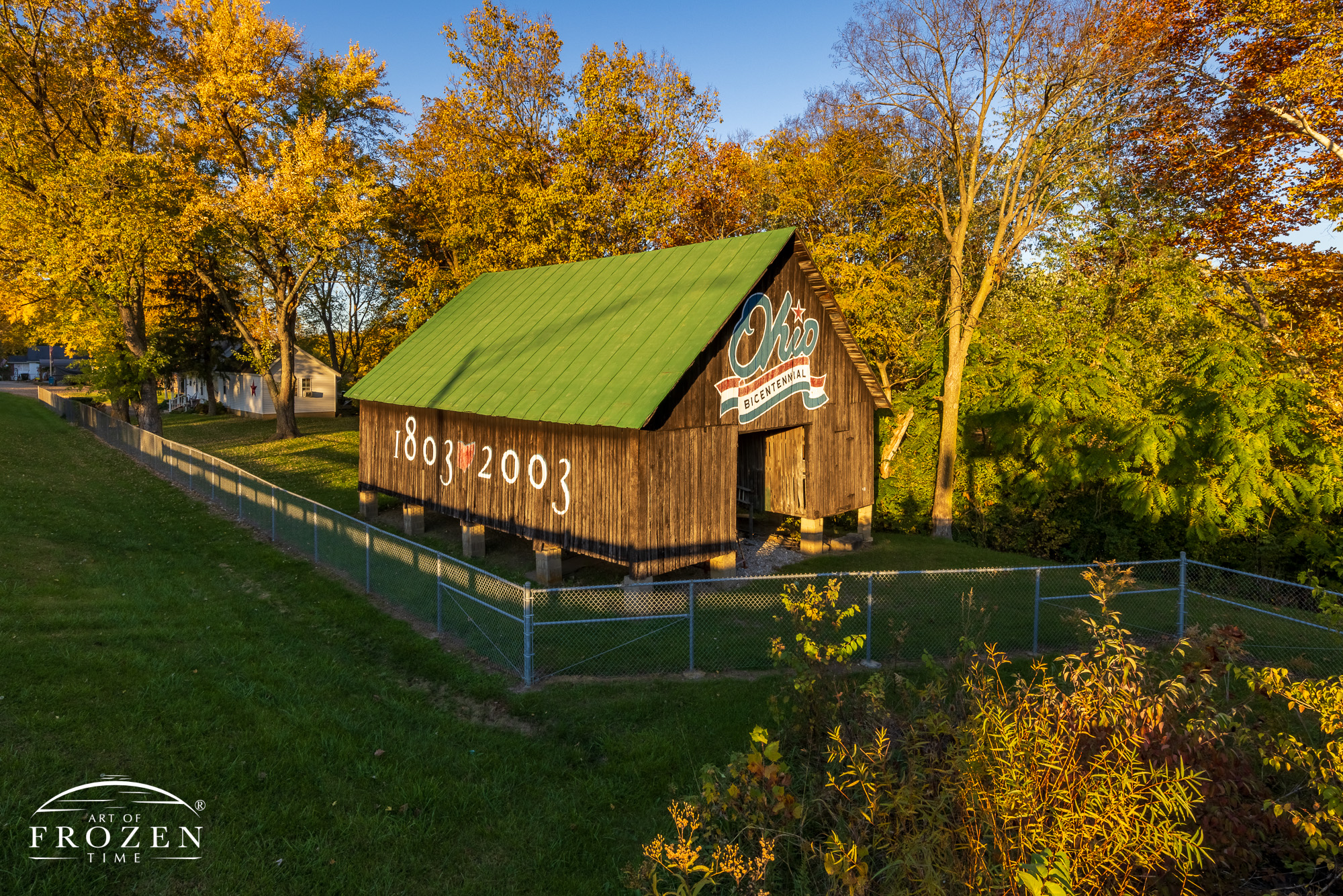 A black barn with a green metal roof displays the Ohio Bicentennial logo on a fall evening where the warm light paints everything in a golden hue