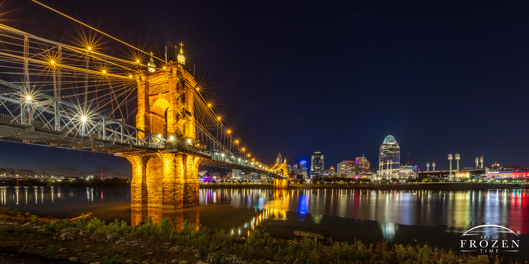 A night view where the Roebling Bridge leads the eye across the Ohio River towards the Cincinnati Skyline