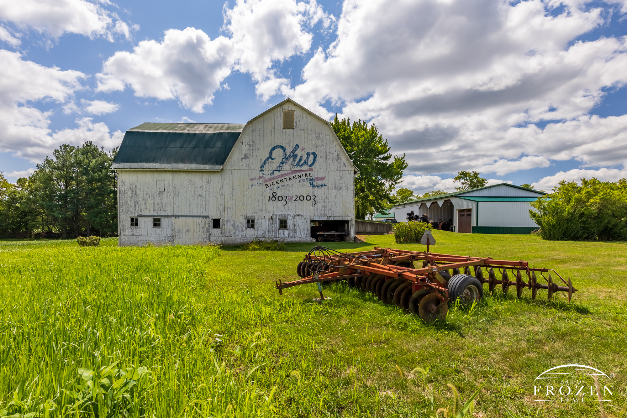 A white double bay barn featuring the Ohio Bicentennial Barn logo on its north side. Given its 25 years, the logo is beginning to fade, adding a nostalgic feeling to the farm