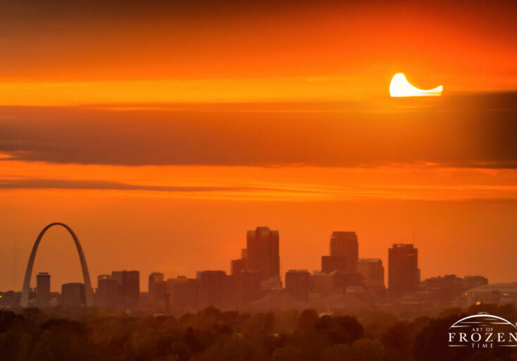 A solar eclipse at sunset over the St Louis skyline and iconic Gateway Arch which briefly appeared between the clouds