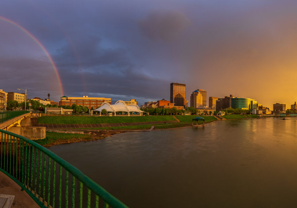 Panorama of the Dayton Skyline where the sun peeks through a sliver of clear air at sunset which produces a full rainbow